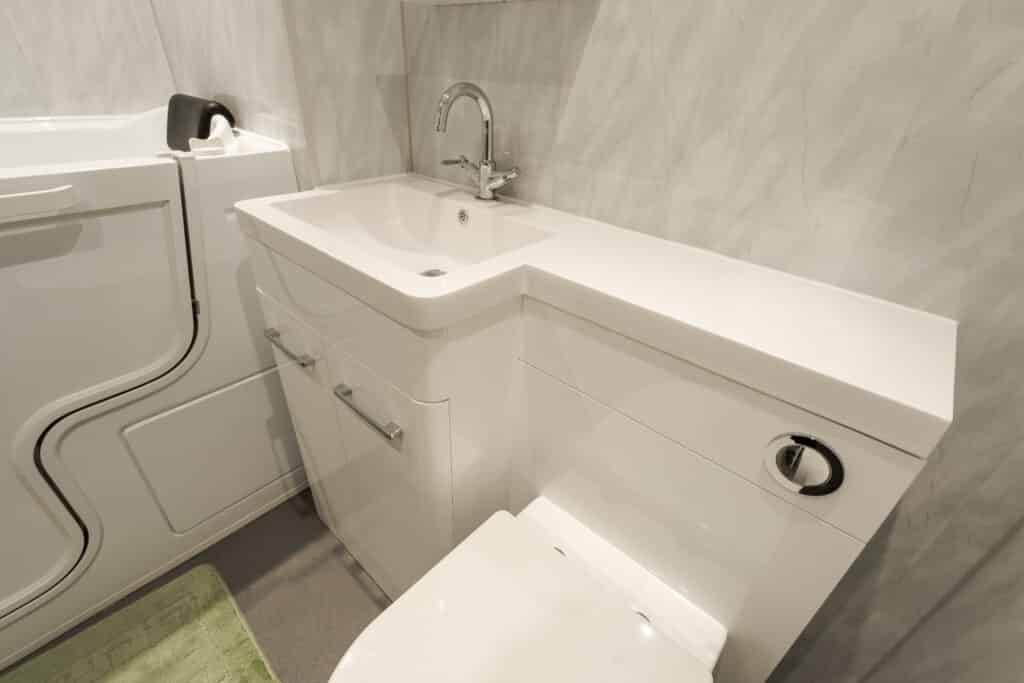 Close-up of a high-gloss white vanity unit with an integrated washbasin and concealed-cistern toilet, installed by Age Care Bathrooms next to a walk-in bath with an easy-access door.