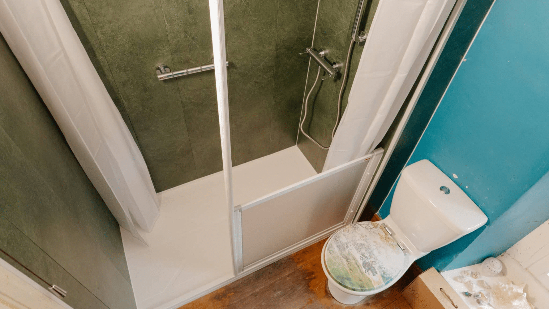 A newly installed, accessible wet room by Age Care Bathrooms, featuring an open level-access walk-in shower on the left, a central modern washbasin with storage, and a low-level toilet in the corner. The room has consistent dark wood-panelled walls and flooring, an obscure glass window, and a chrome ladder towel rail, demonstrating a complete and dignified home adaptation.