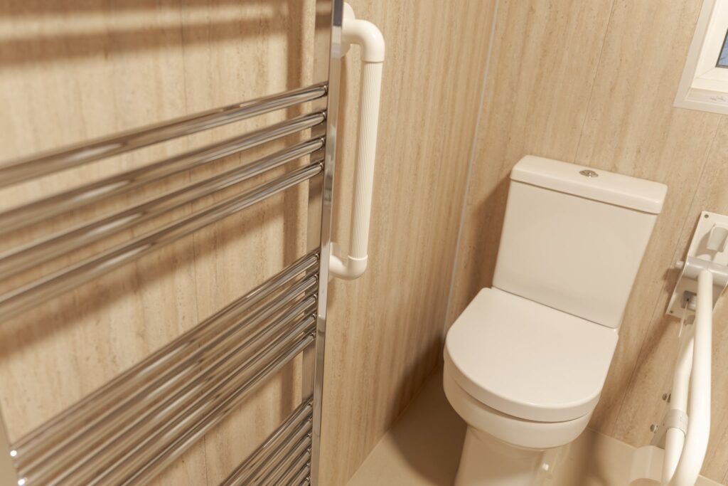 Samantha's toilet with a drop-down support arm, beside the chrome heated towel rail and a grab rail.