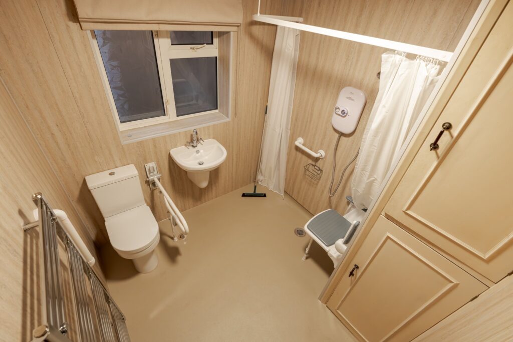 Samantha's finished wet room: level-access shower with padded seat, easy-reach basin, supported toilet and heated towel rail.