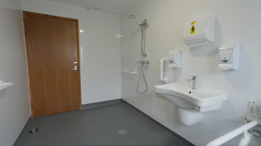 The open shower area in Stella's wet room, with grab rails, a handheld shower and level anti-slip flooring.