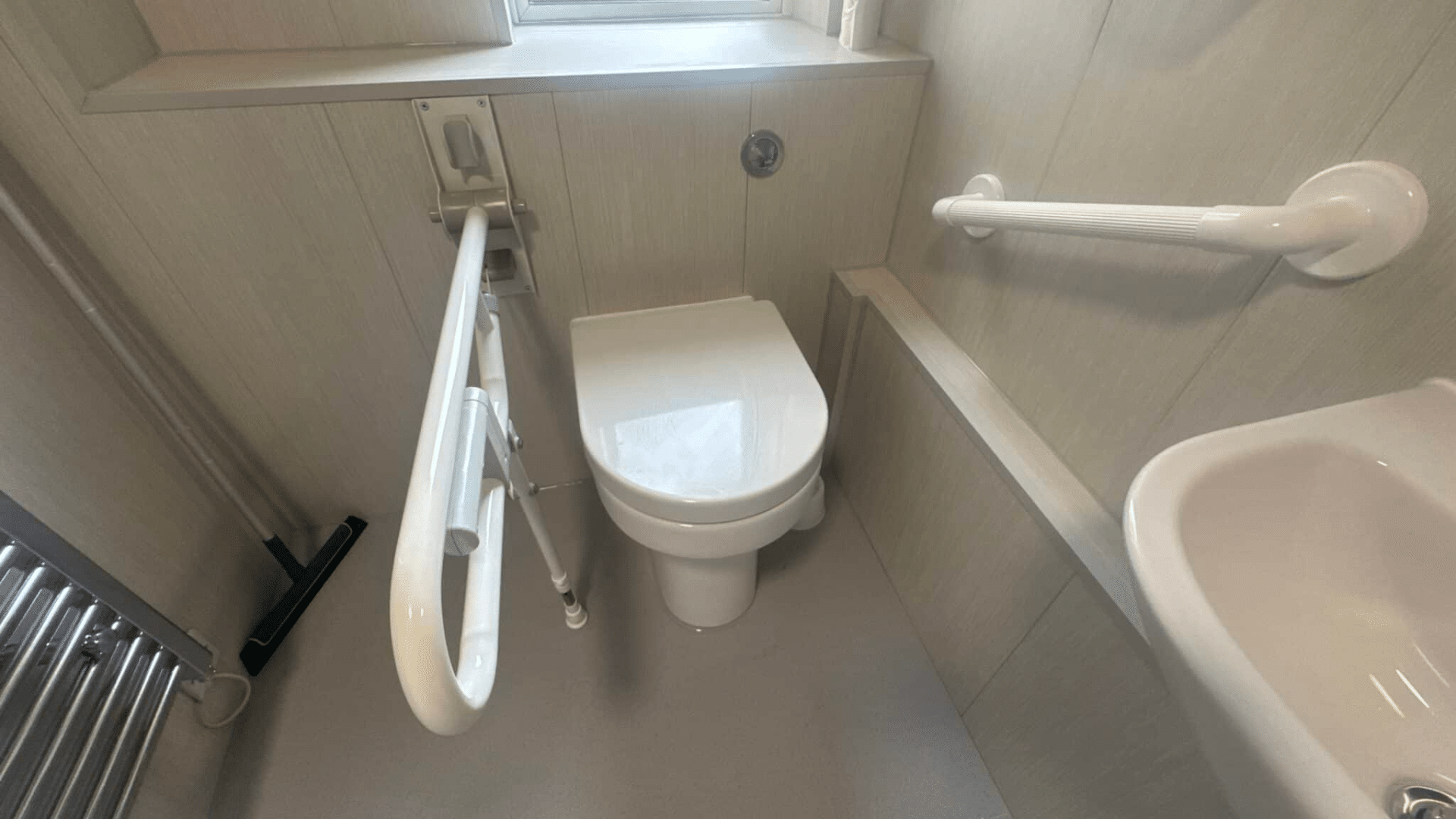 Drop-down grab rail and wall-mounted rail next to the toilet area. By Age Care Bathrooms.