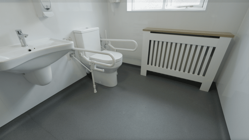 White drop-down grab rails around the toilet, part of a wet room installation by Age Care Bathrooms.