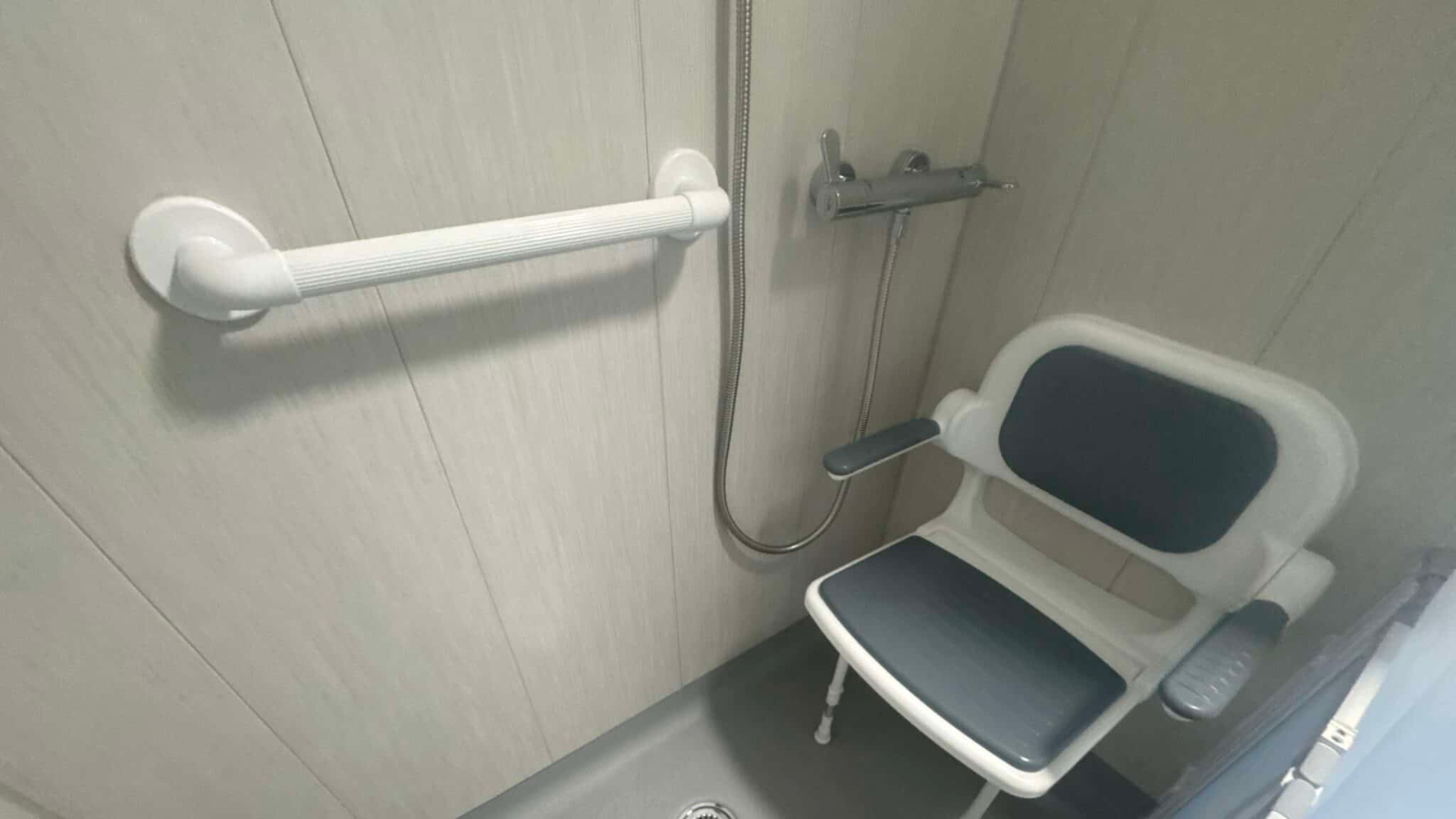 White plastic grab rail fitted in the shower area of a wet room. Installed by Age Care Bathrooms.