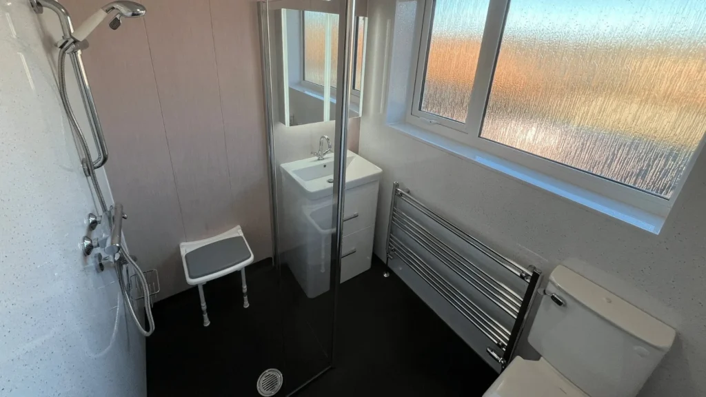 Level-access wet room by Age Care Bathrooms, with a fold-down shower seat and riser rail shower.