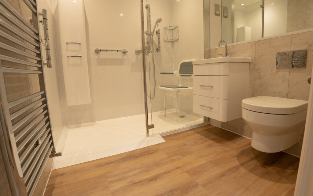 Maya's new walk-in shower with its low entry, glass screen and fold-down seat, with the retained heated towel rail nearby.