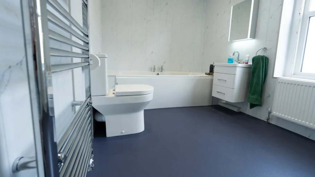 Peter's new wet room with a bath, toilet, wall-hung basin and navy slip-resistant floor.