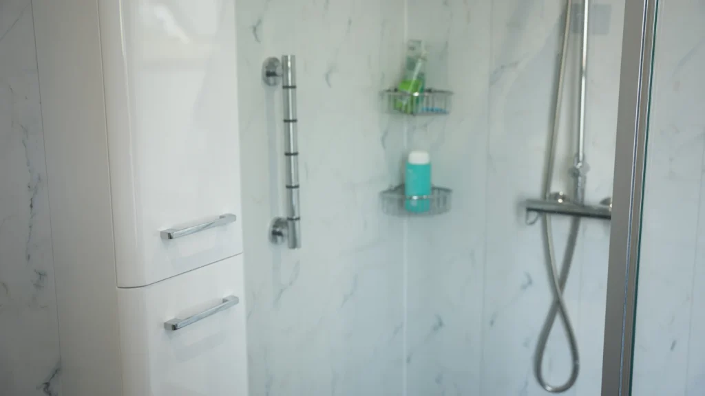 Walk-in shower in Peter's wet room, with a grab rail, handset and marble-effect walls.