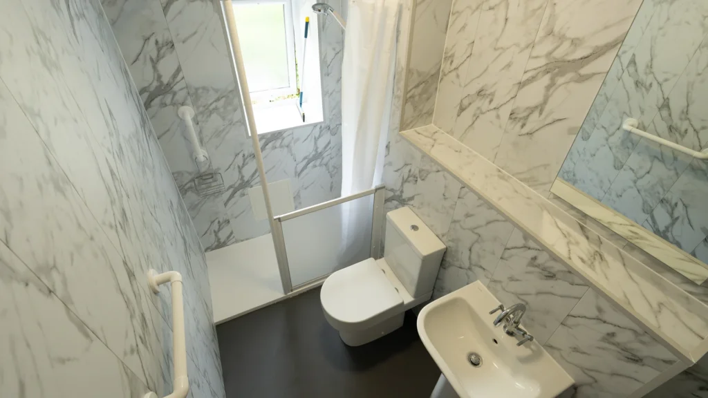Adrian's walk-in shower with a half-height care screen, toilet, basin and grab rails
