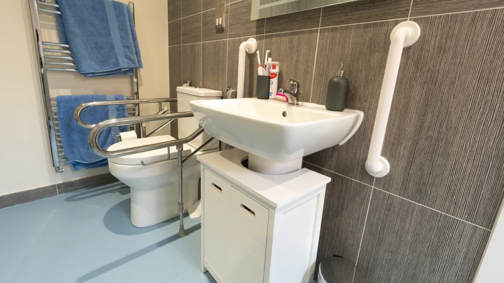 Toilet with drop-down grab rails and a basin in Charlotte's accessible wet room