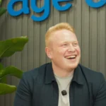 Sam Davies, founder of Age Care Bathrooms, smiling in front of the Age Care sign at our office.