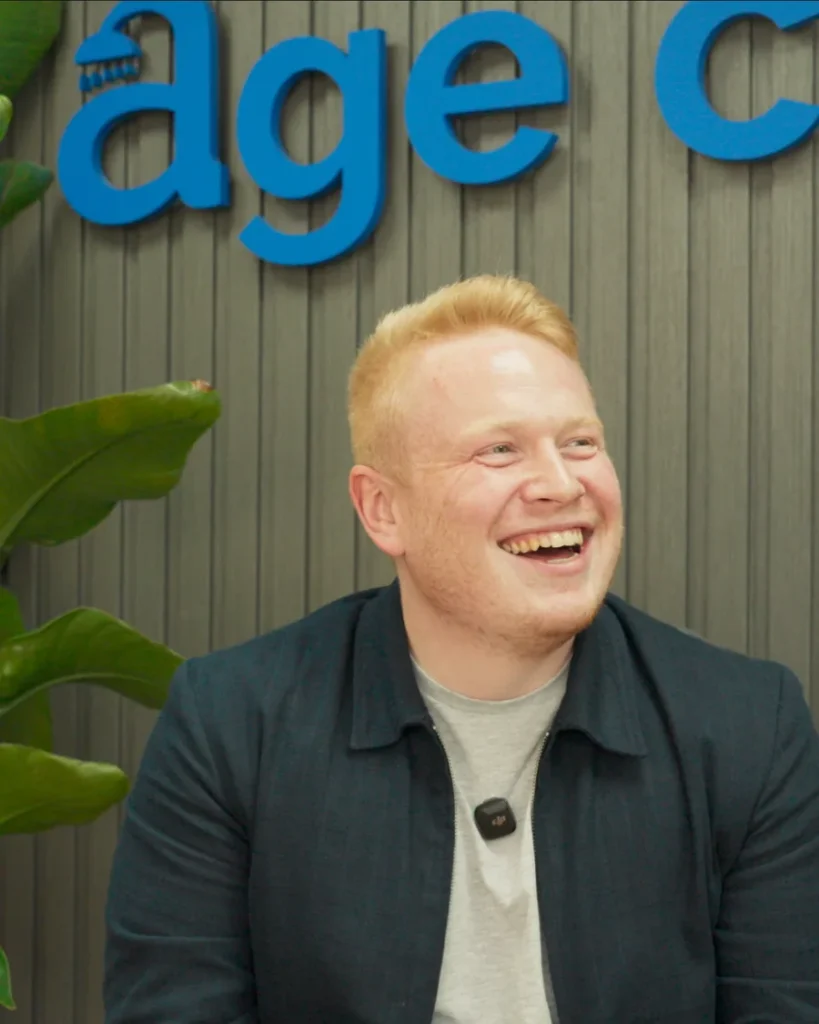 Sam Davies, founder of Age Care Bathrooms, smiling in front of the Age Care sign at our office.