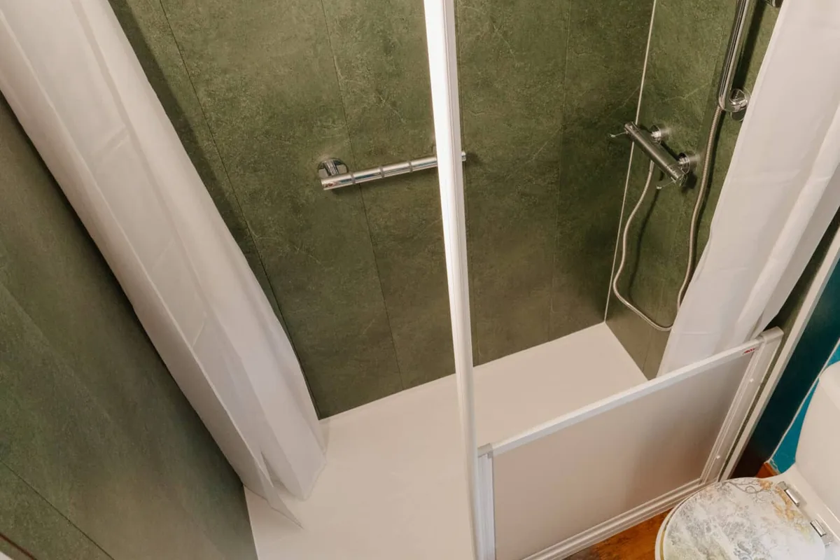 Denise’s walk-in shower with green wall panels, a half-height screen, curtains, a thermostatic shower on a riser rail and a grab rail