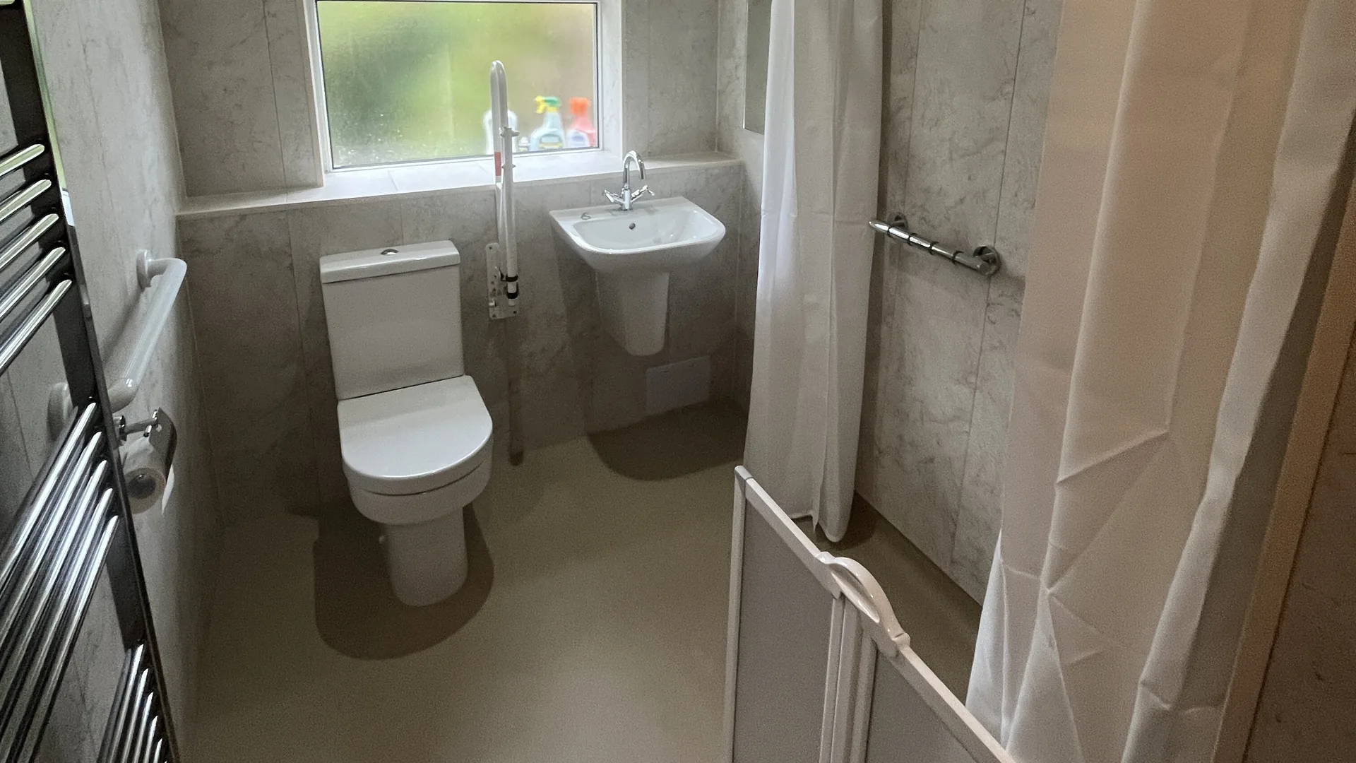 Finished disabled wet room with half-height shower doors, a level floor, WC and basin.
