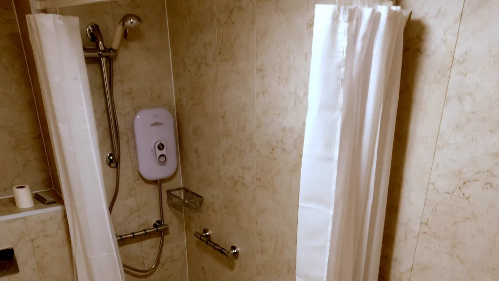Level-access shower with an electric shower, riser rail and grab rails in Malcom's bathroom