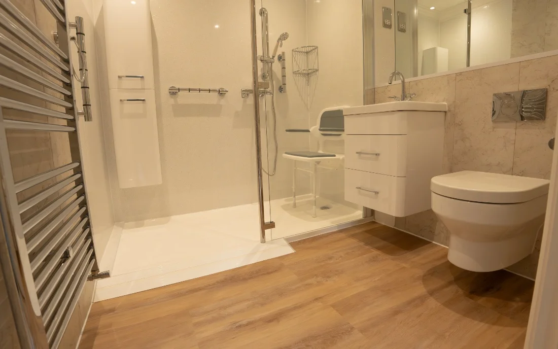 Maya’s walk-in shower: a low, anti-slip tray, a glass screen, wall panels, a shower seat, grab rails and a shower on a riser rail