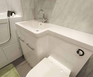 Close-up of a high-gloss white vanity unit with an integrated washbasin and concealed-cistern toilet, installed by Age Care Bathrooms next to a walk-in bath with an easy-access door.