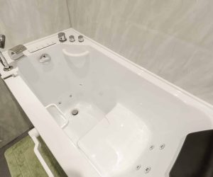 High-angle close-up of a luxury walk-in whirlpool bath installed by Age Care Bathrooms, featuring a black padded headrest, integrated spa jets, a hand-held shower attachment, and chrome controls.