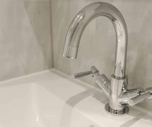 Close-up of a high-neck chrome swan-neck mixer tap with easy-to-operate lever handles, installed on a white washbasin by Age Care Bathrooms.