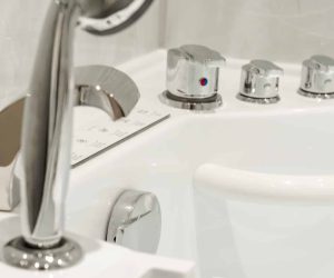Close-up of a chrome handheld shower head attachment and deck-mounted mixer taps on a white walk-in bath by Age Care Bathrooms.